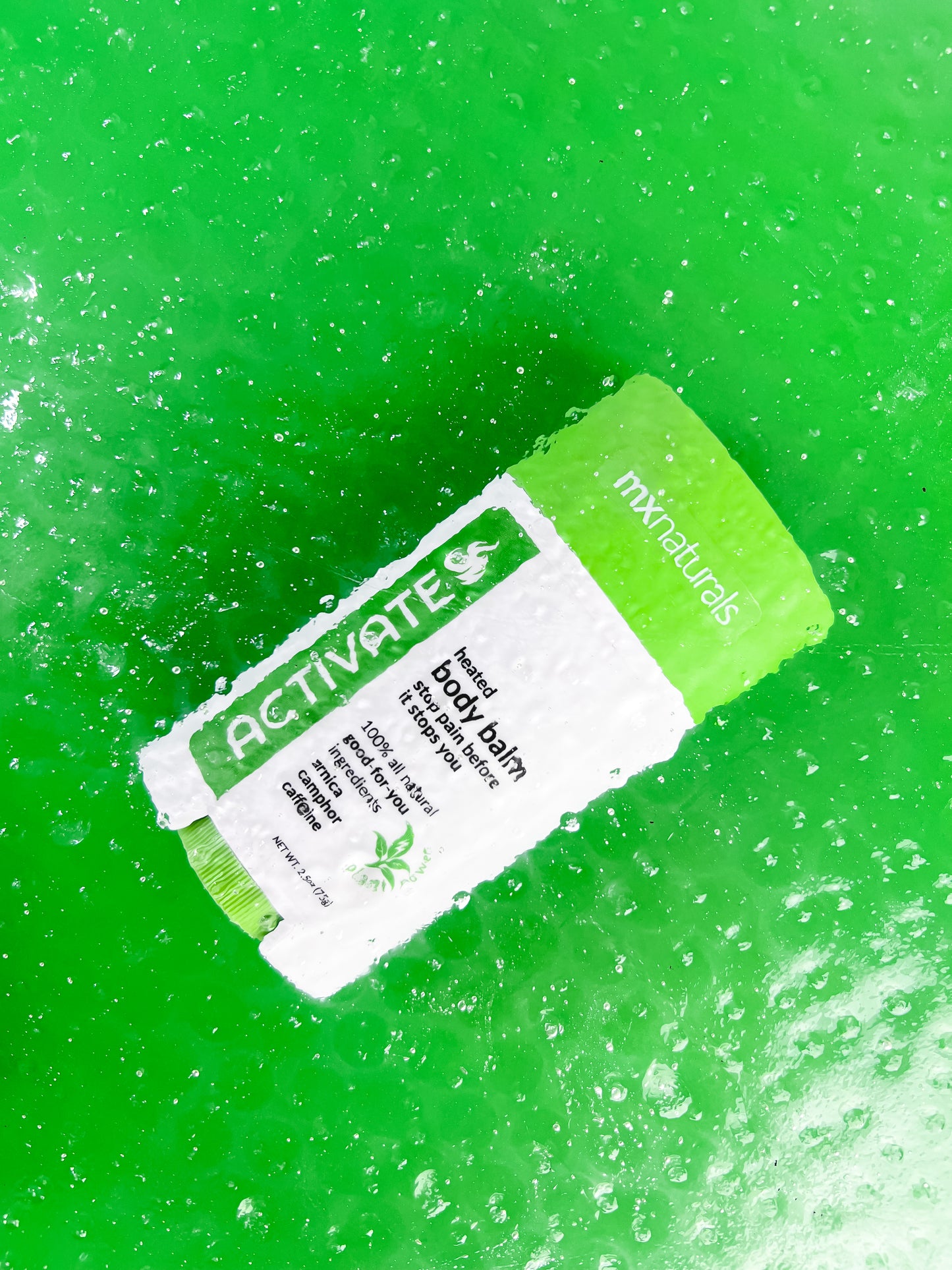a white and green product titled "activate heated body care balm"  is submerged under hot, sweating water to represent the heat of the product on a green background..