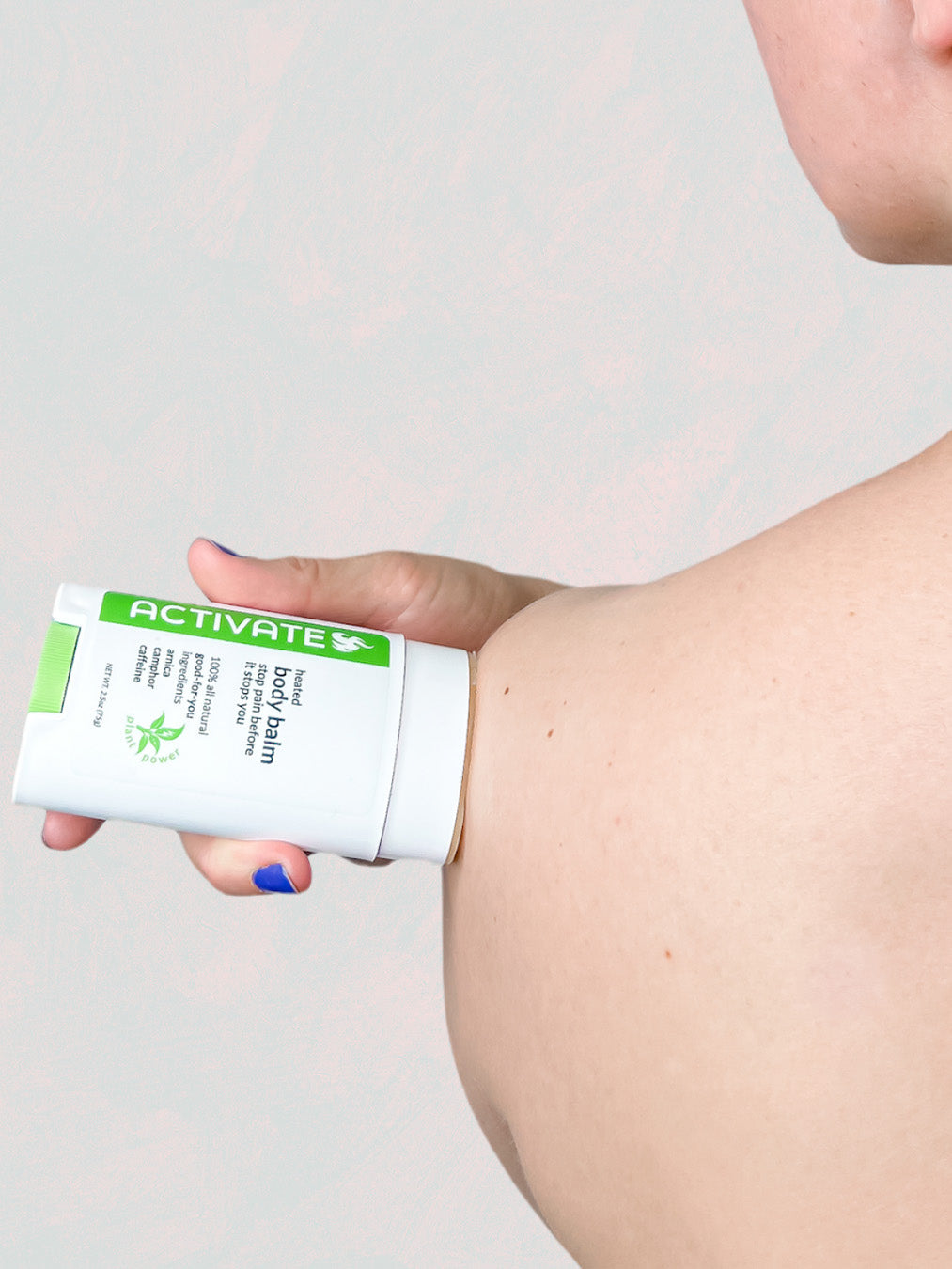 caucasian female applying a green and white product titled "activate pain relief body balm" onto left shoulder prior to activity to prevent further injury.