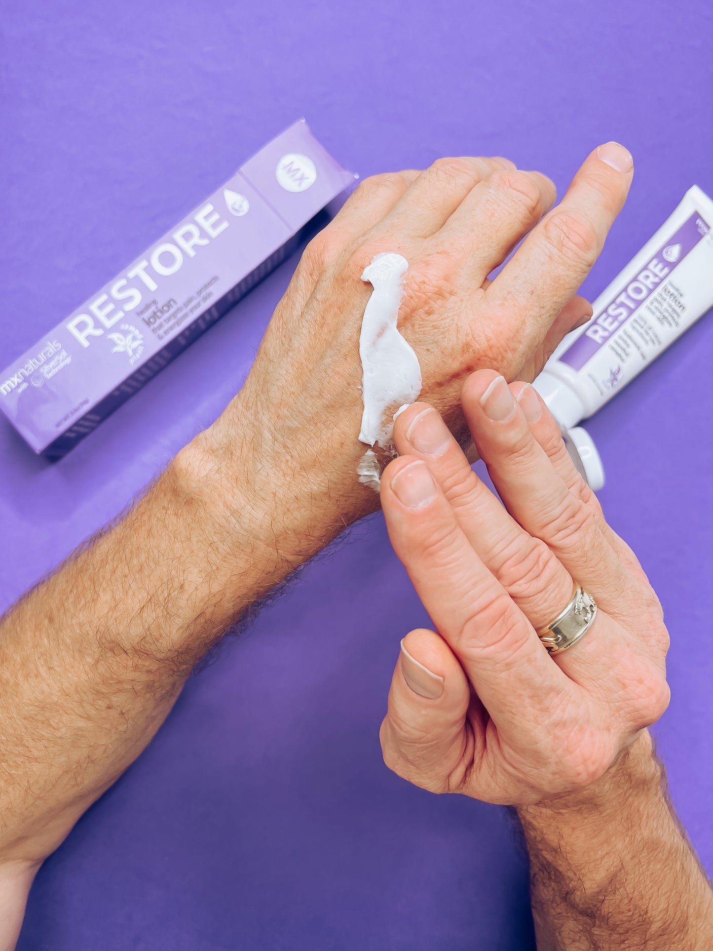 caucasian male hands applying a purple and white, "restore targeted pain relief healing and moisturizing lotion" onto a sore, arthritic hands to relieve the arthritis pain.